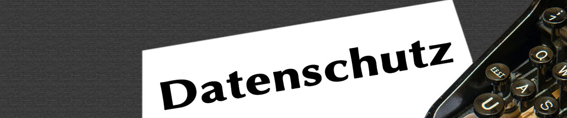 Es ist ein Schreibtisch mit schwarzer Oberfläche in der Draufsicht zu sehen. Rechts im Anschnitt befindet sich eine alte Schreibmaschine. Quer übers Bild befindet sich ein weißes Schild mit der Aufschrift Datenschutz