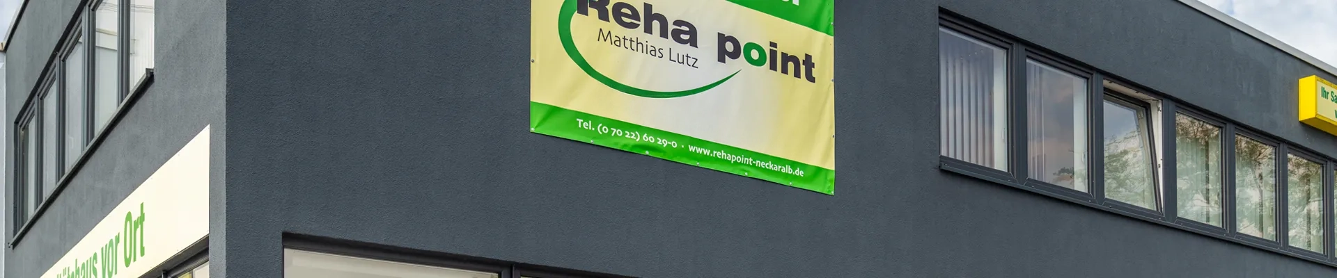 Bild Gebäude Reha point in Nürtingen. Es ist eine graue Fassade mit dem gelben Logo von Reha point. Zu sehen ist die oberste Etage